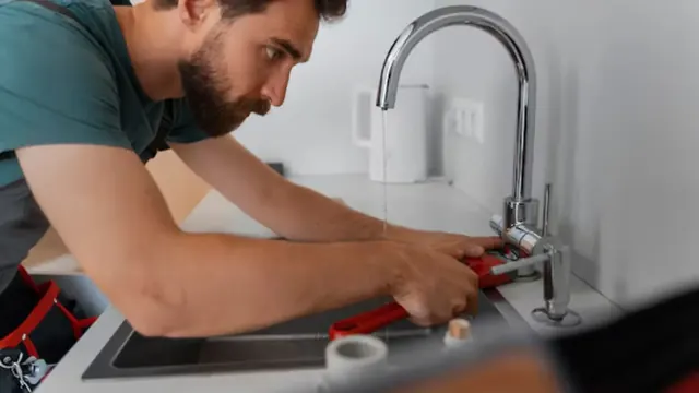 Plumber tightening a kitchen faucet with a wrench